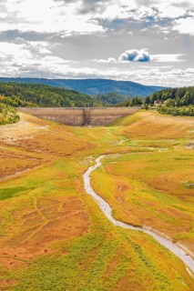 A dry valley with a dam in the background and a narrow river through the meadows, rehabilitation of