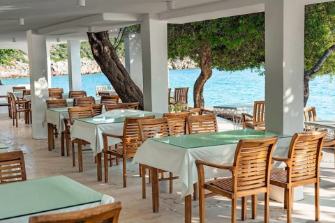 Rattan chairs and tables set on a seaside terrace overlooking clear blue water on a bright and