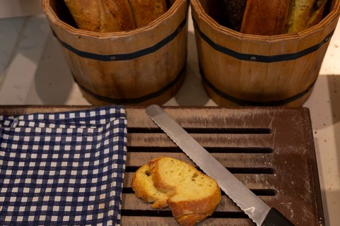 Sliced bread rests on a wooden cutting board next to a knife, with baskets of whole loaves in the
