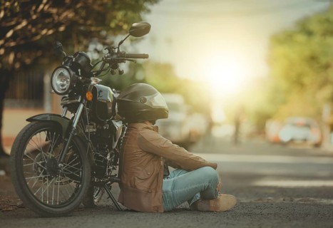 Portrait of a young motorcyclist sitting on the road, leaning against his motorcycle. Male biker