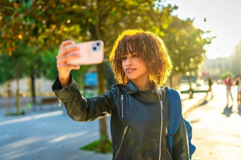 Latin young woman taking photos of the city using mobile phone during sunset
