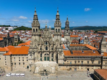 The aerial view shows an imposing cathedral with red roofs and historical flair under a blue sky,