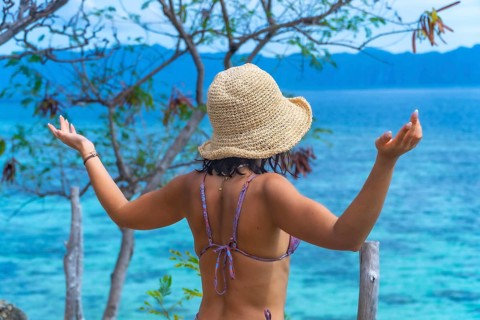 Young woman wearing a sun hat enjoying breathtaking view of turquoise ocean during her vacation on
