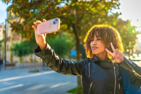 Beauty latin woman with curly hair gesturing success while taking selfie in the city during sunset