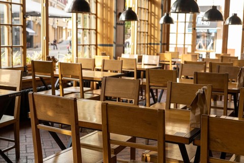 The interior of a cozy cafe features rows of simple wooden chairs and tables bathed in warm,