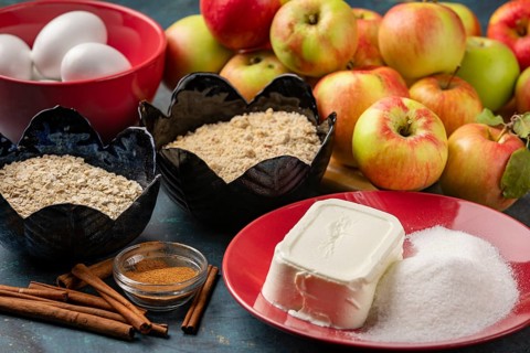 Baking ingredients such as apples, sugar, oats, quark, nuts, eggs and cinnamon on a dark table