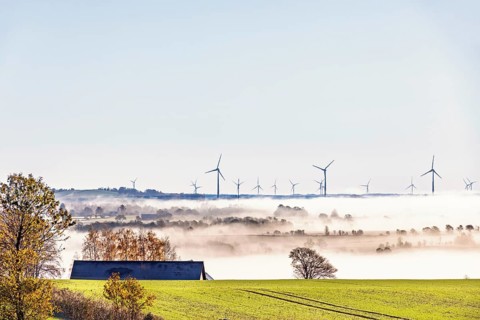 Wind turbines emerges above morning fog stretching across the countryside. Rolling farmland,