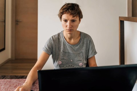 A woman in home clothes works at home at laptops with a tense look, A woman with short hair sits