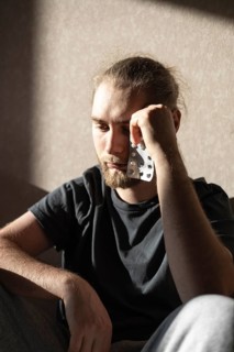 Young man with a beard thoughtfully holding a blister pack of pills. Sitting in a room, he appears
