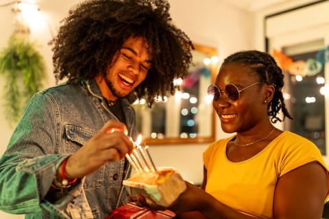 Multi-ethnic friends lighting birthday cake's candles preparing a surprise at home during party at