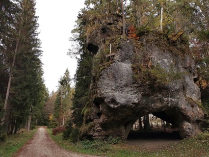 Massive rock in a wooded area flanked by tall conifers next to a path, Großer Lochstein,
