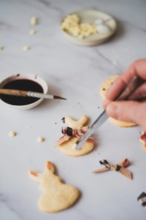 From above, a cropped unrecognizable person delicately paints Easter bunny shaped cookies with