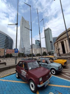 Skyscrapers against cloudy sky, with Fiat 126 cars ready for sightseeing in the foreground and