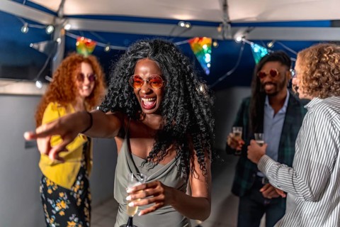 African woman wearing stylish night dress and sunglasses pointing ahead dancing with friends at