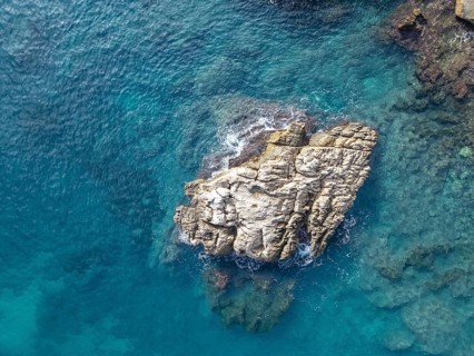 An aerial view captures a rugged rocky outcrop surrounded by clear azure waters of the