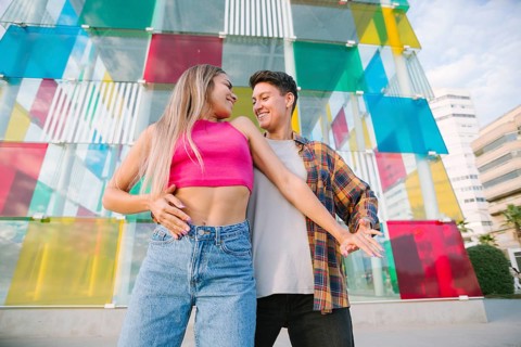 A joyful lesbian couple dances together, smiling and sharing a playful moment. The vibrant glass