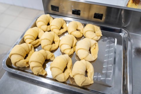 Raw unbaked croissants arranged on a metal tray, ready for baking in a professional bakery kitchen,