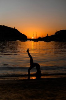 A silhouette of a child performing an acrobatic pose by the sea during sunset in Soller, Majorca.