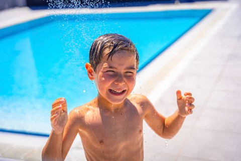 Close-up portrait of a caucasian wet boy smiling at camera playing on the pool alone