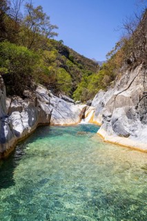 Clear turquoise water at the base of a smooth natural rock slide surrounded by canyon walls and