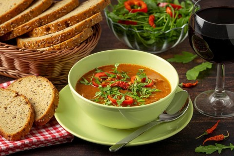 Goulash decorated with paprika and arugula, served with bread and red wine