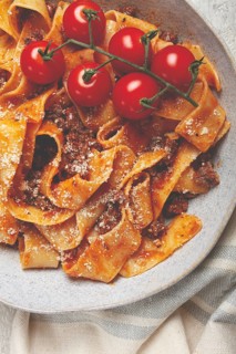 Pappardelle pasta with bolognese sauce, topped with parmesan cheese and cherry branch, homemade, no