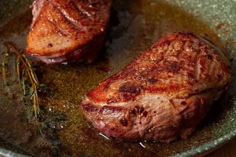 Cooking duck breast, in a frying pan, fried, with spices and herbs, close-up, no people
