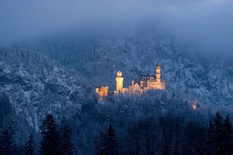 Snow-covered castle, illuminated at dusk, embedded in misty mountains, Neuschwanstein, Schwangau,