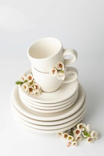 Neatly arranged spring tableware set featuring stacked white ceramic plates and cups, each adorned