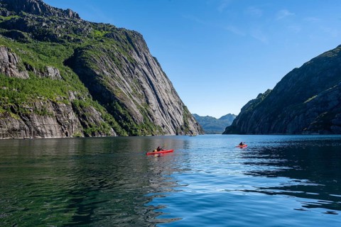 Two kayakers with red kayaks in the fjord Trollfjord, mountains reflected in the water, fjord