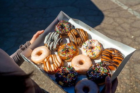 Person holding an open box filled with a variety of sweet donuts, featuring different flavors of