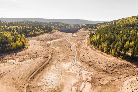 Extensive dry riverbed with surrounding forests and autumnal hills, emptied Schwarzenbach dam,