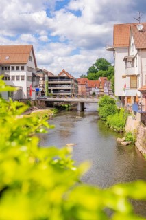 River flows under bridge surrounded by colorful buildings and lush vegetation, Calw, Black Forest,