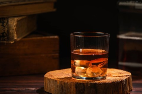 Glass of whiskey with ice cube cubes on wood in a cozy setting