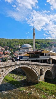 View of a bridge across a river, Prizren Bistrica with mosque in the background and wooded hills,