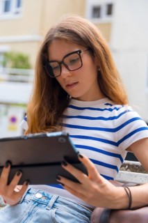 Young woman concentrating on a digital tablet while sitting outside, engaging with technology for