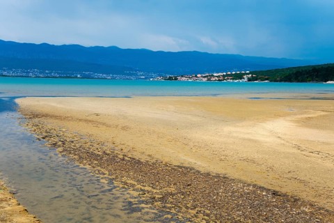Wide beach landscape with watercourse, mountains in the background and a village along the coast