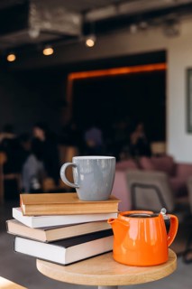 A cozy coffee shop scene with a grey mug placed on a stack of books, accompanied by an orange