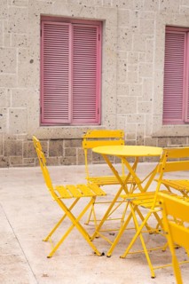 A cozy outdoor setting features vibrant yellow chairs and a table against a textured stone wall
