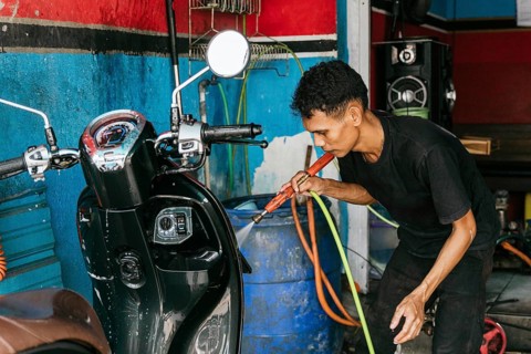 A man diligently cleans a motorcycle using a hose in a garage setting. The background features