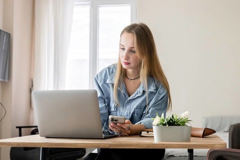 A woman sits on a couch in a living room. She works on a laptop with focus. A blanket and some