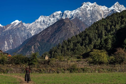Elderly woman, local people of the Tsumba Tibetan ethnic group on dirt road in front of snow-capped