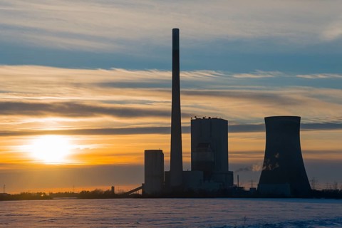 Industrial site at sunset, with chimney and cooling tower, surrounded by clouds, coal-fired power