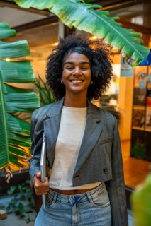 Vertical portrait of a happy african woman holding laptop at the coworking entrance