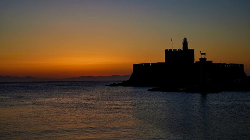 Fortress as dark silhouette with calm sea, sunrise, dawn, Fort of Saint Nikolaos, Mandraki harbour,