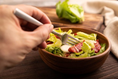 Mixed salad with lettuce, tomatoes, onion and vegetables in wooden bowl with hand on brown wooden