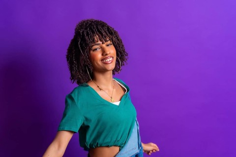 Carefree young latin woman with curly hair dancing, wearing a green t shirt and denim jacket on a