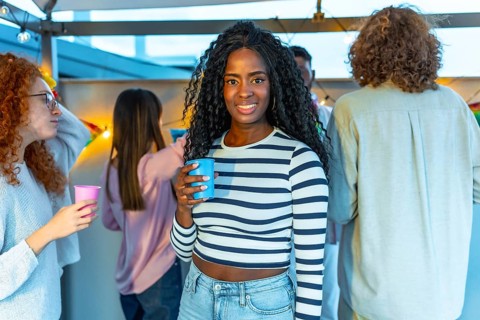 Beauty african woman with long curly hair smiling standing in a roof party with multi-ethnic