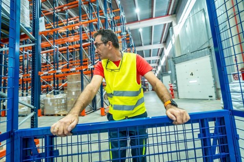 Frontal view of a mature man wearing safe reflective waistcoat in a distribution warehouse