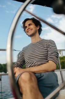 A man enjoys a serene afternoon on a sailboat. The scene captures a relaxed mood with a backdrop of